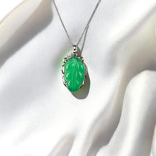 Green jade pendant on a silver chain against a white fabric background