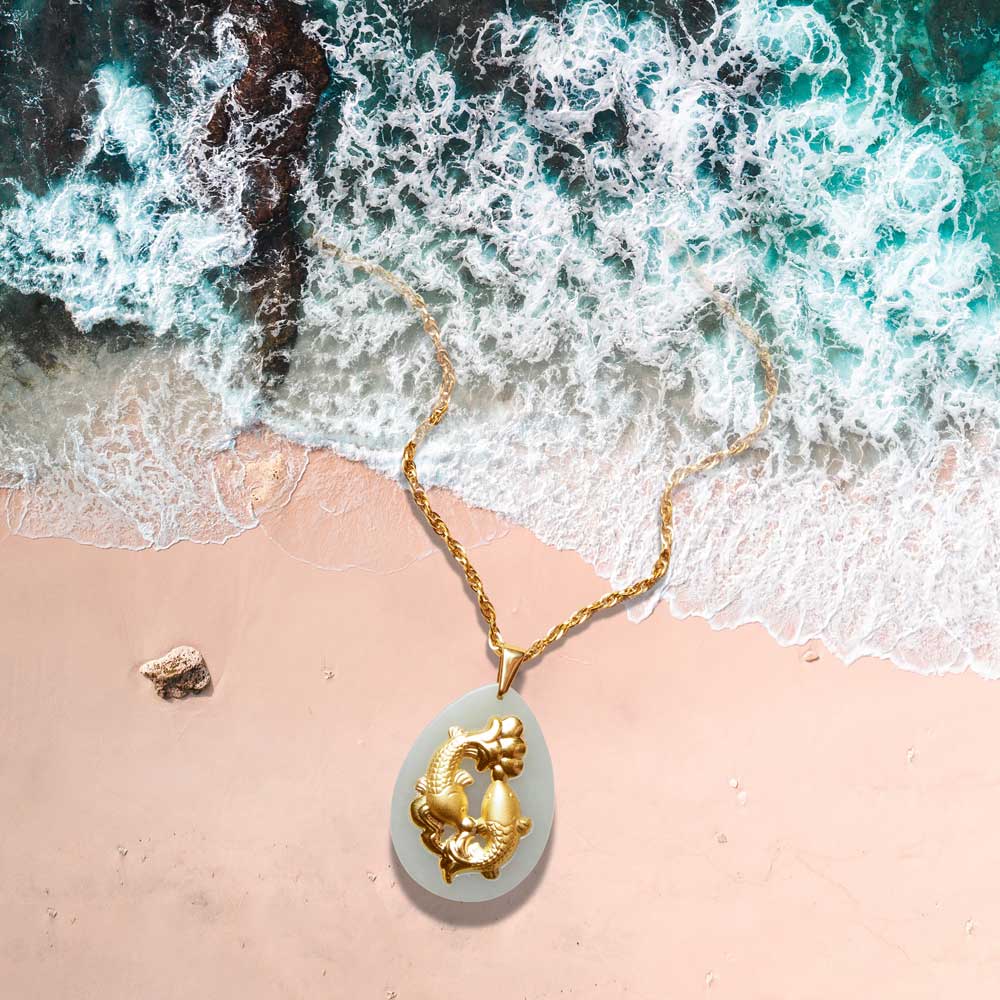 Gold necklace with a pendant on a beach with waves in the background