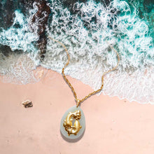Gold necklace with a pendant on a beach with waves in the background