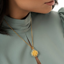 Gold necklace with a floral pendant worn by a person in a light gray outfit, with 'Marrelin' brand visible.