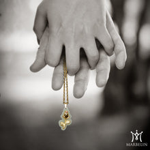 Close-up of hands holding a gold necklace with a pendant against a blurred background