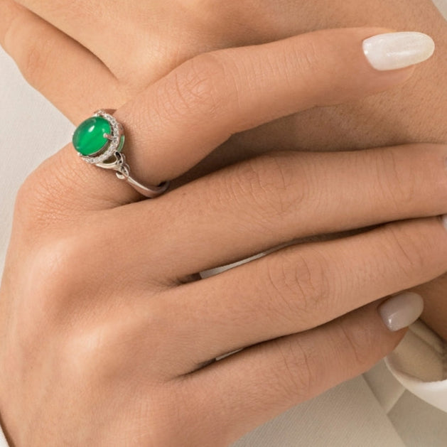 Close-up of hands wearing green gemstone rings with a visible brand logo.