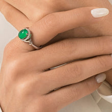 Close-up of hands wearing green gemstone rings with a visible brand logo.