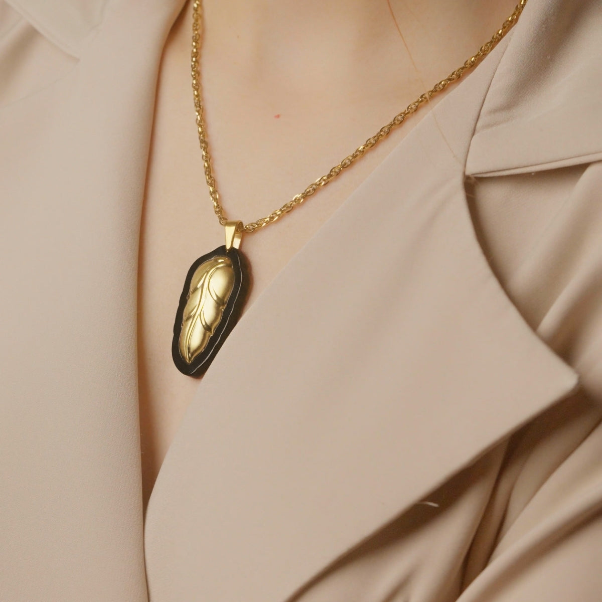 Gold necklace with a black pendant on a beige outfit