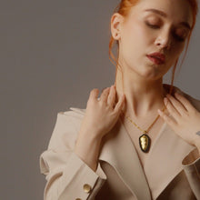 Woman wearing a gold necklace with a pendant against a neutral background