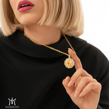 Woman wearing a gold necklace with a pendant, pointing to it.