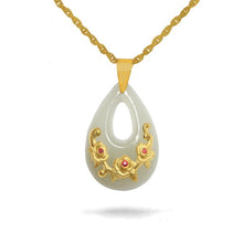 Teardrop-shaped pendant with gold floral designs and red stones on a white background